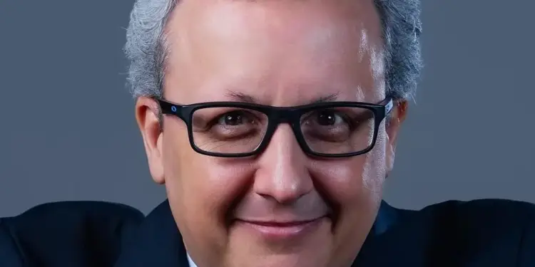 Primer plano de un hombre maduro con gafas, cabello gris y traje oscuro mirando a la cámara.