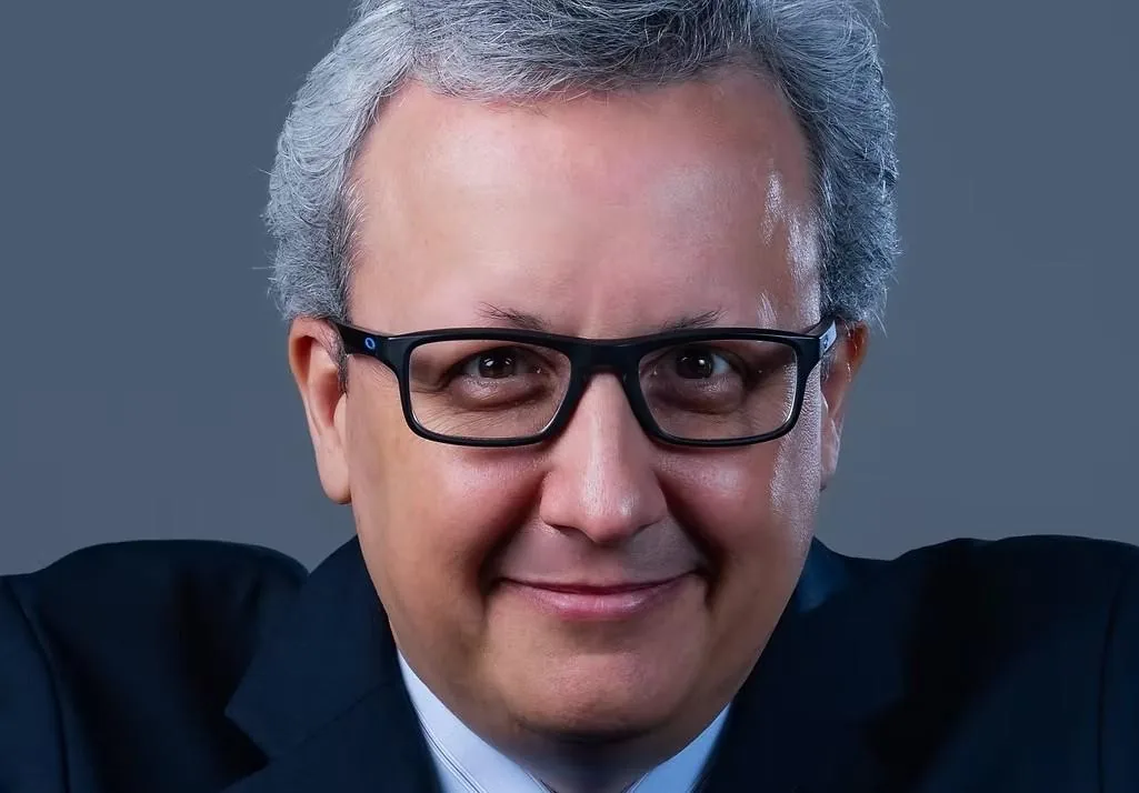 Primer plano de un hombre maduro con gafas, cabello gris y traje oscuro mirando a la cámara.