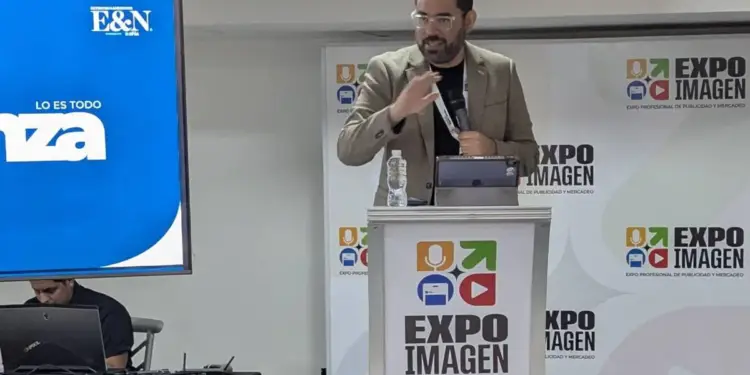 Hombre dando una conferencia de marketing y negocios en un podio de Expo Imagen con pantalla azul de fondo.