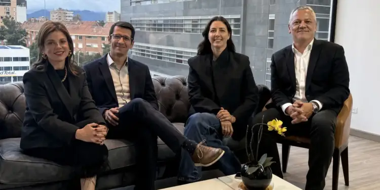 Cuatro profesionales sentados en una sala de reuniones corporativa con ventanales grandes y vista a la ciudad.