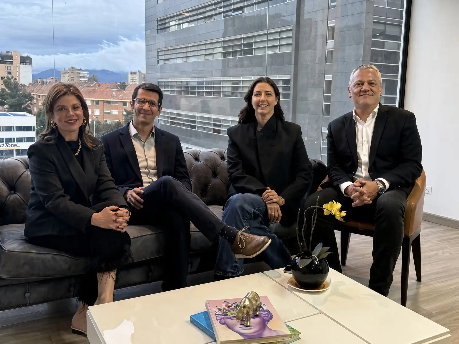Cuatro profesionales sentados en una sala de reuniones corporativa con ventanales grandes y vista a la ciudad.