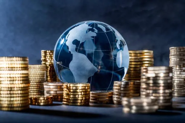 Esfera de cristal con forma de globo terráqueo rodeada por múltiples pilas de monedas doradas sobre fondo oscuro.