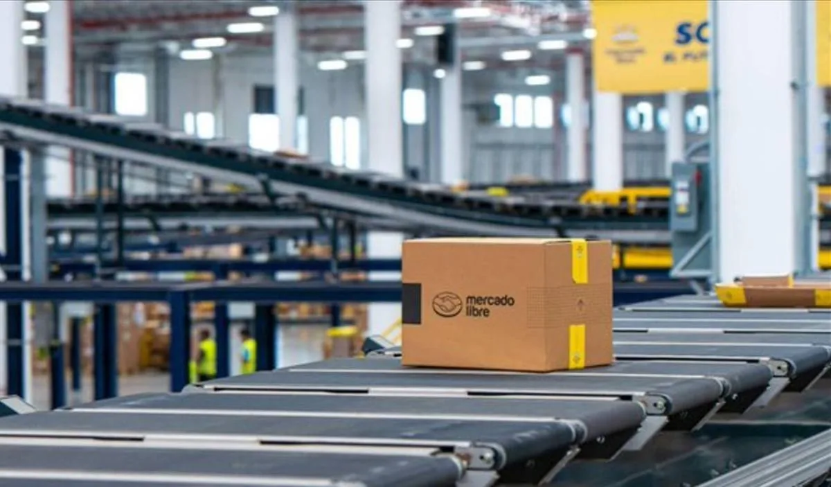 Caja de cartón con el logo de Mercado Libre sobre una cinta transportadora en un centro de distribución logístico.