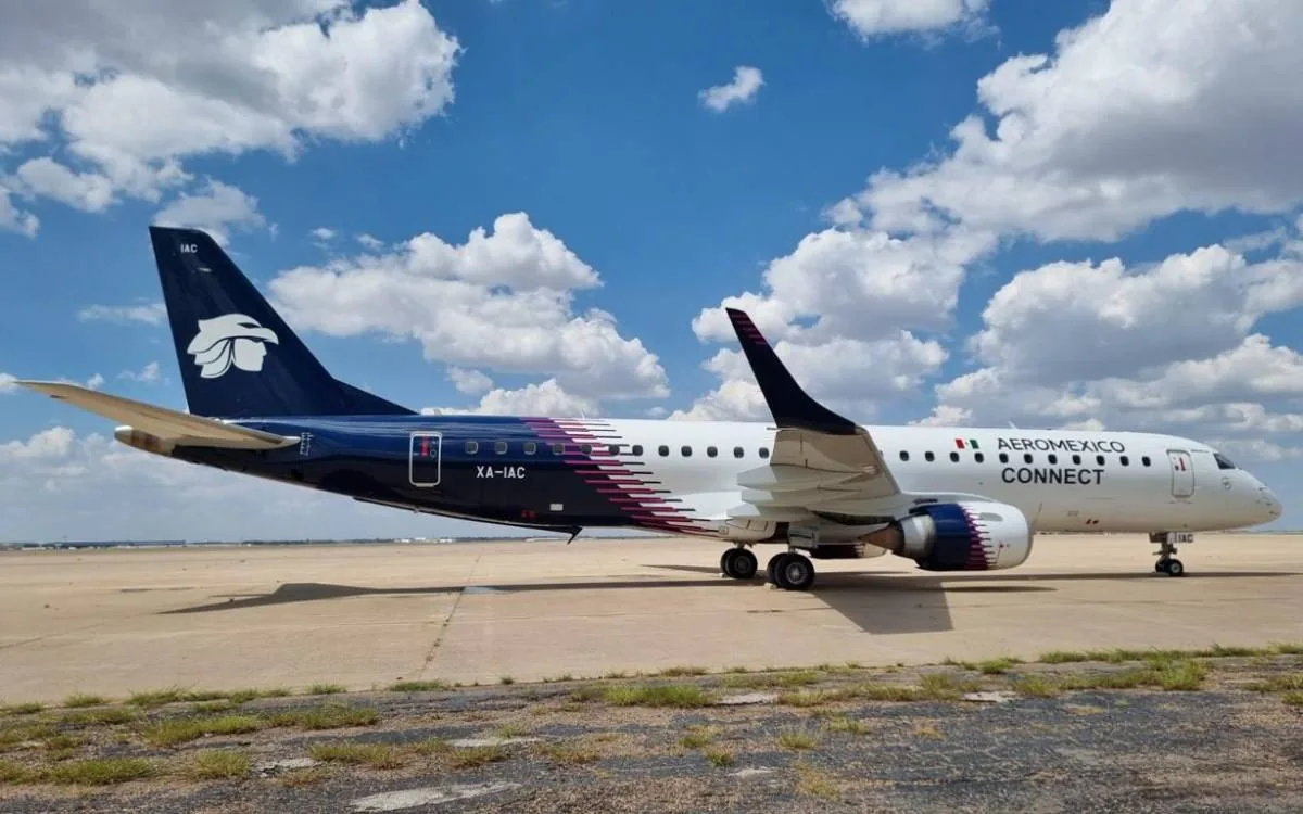 Avión comercial Aeroméxico Connect con matrícula XA-IAC estacionado en una pista de concreto bajo un cielo azul con nubes blancas y esponjosas.