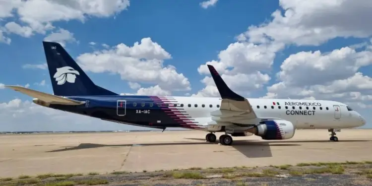 Avión de pasajeros Aeroméxico Connect, blanco y azul oscuro con franjas rosas, estacionado en una pista bajo cielo nublado.