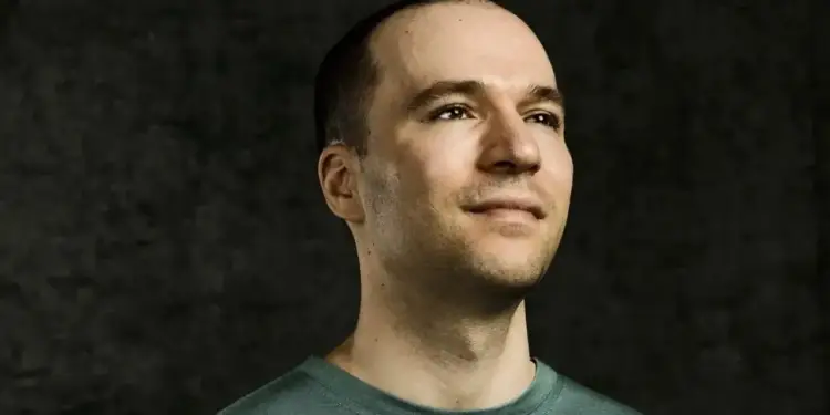 Primer plano de un hombre con camiseta verde mirando hacia arriba con expresión seria y pensativa ante un fondo oscuro.