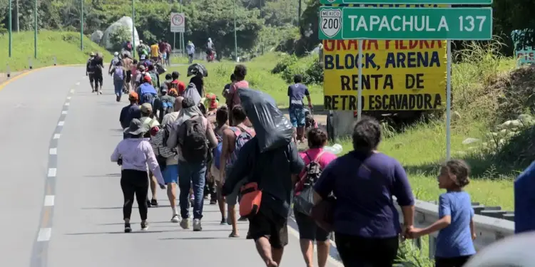 Grupo de personas caminando a pie por la orilla de una carretera junto a señales de tránsito en México.