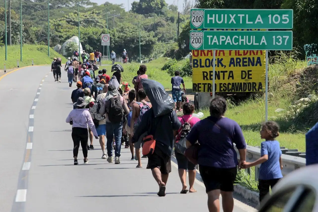 Grupo de personas caminando a pie por la orilla de una carretera junto a señales de tránsito en México.