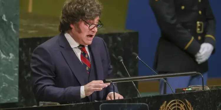 Hombre de traje hablando en un podio con micrófono y emblema oficial.