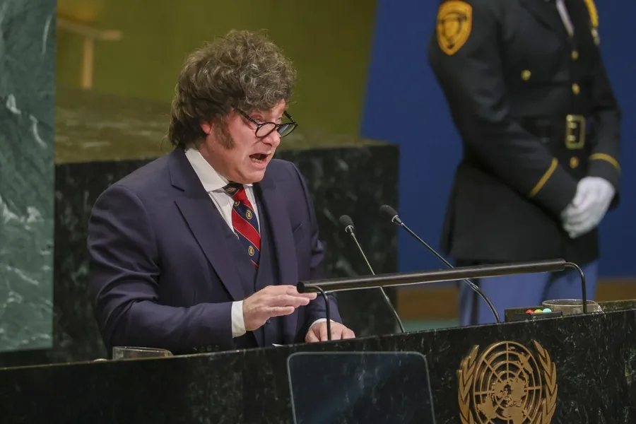 Hombre de traje hablando en un podio con micrófono y emblema oficial.