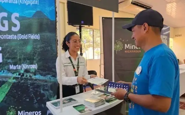 Una representante en un stand de Mineros Nicaragua entrega folletos a un visitante en un evento corporativo.