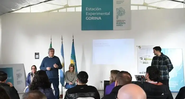Un hombre de pie hablando frente a una audiencia en una sala de conferencias con un cartel de Estación Experimental GORINA.