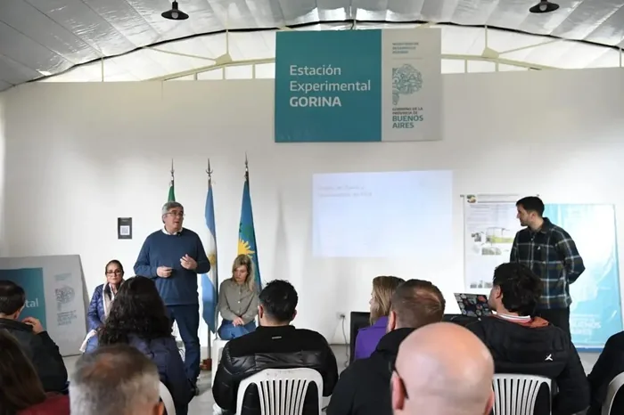 Un hombre de pie hablando frente a una audiencia en una sala de conferencias con un cartel de Estación Experimental GORINA.