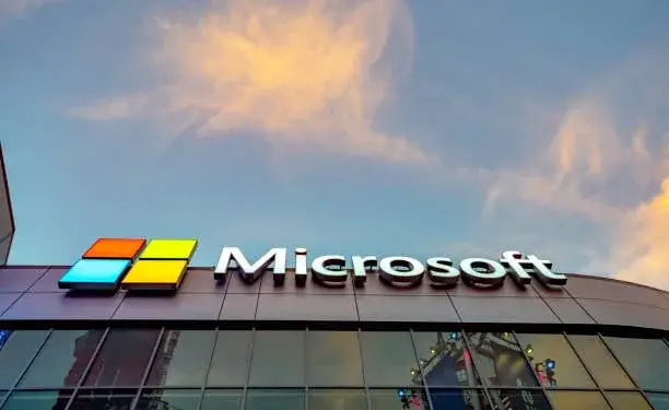 Letrero y logotipo de Microsoft en la fachada de un edificio corporativo bajo un cielo nublado al atardecer.