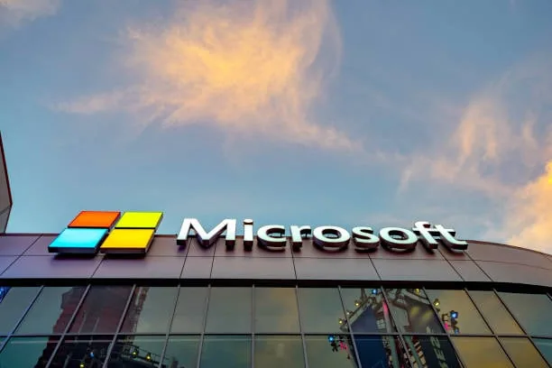 Letrero y logotipo de Microsoft en la fachada de un edificio corporativo bajo un cielo nublado al atardecer.