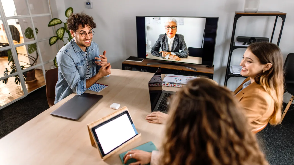 Equipo de profesionales reunidos alrededor de una mesa de madera participando en una videoconferencia.