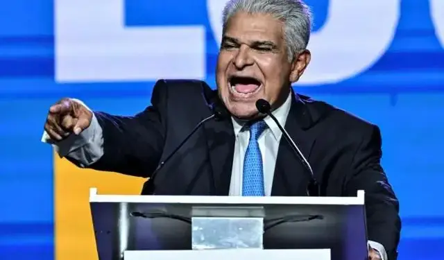 Hombre maduro con traje y corbata hablando apasionadamente frente a un atril en un evento corporativo.