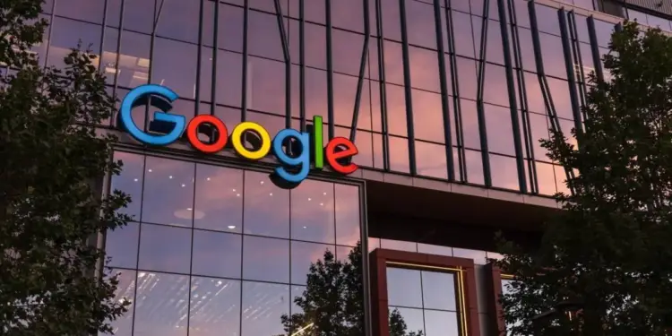 Fachada de cristal de un edificio de oficinas moderno con el logo de Google en colores vibrantes, reflejando un cielo al atardecer.