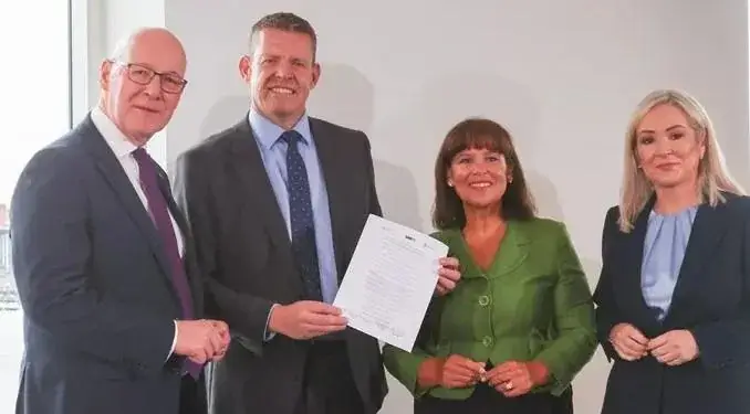 Cuatro profesionales sonriendo mientras sostienen un documento firmado en una reunión de negocios.