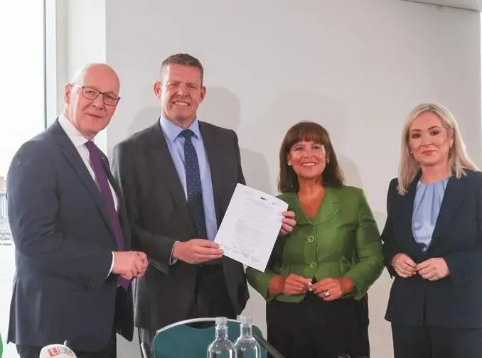 Cuatro profesionales sonriendo mientras sostienen un documento firmado en una reunión de negocios.