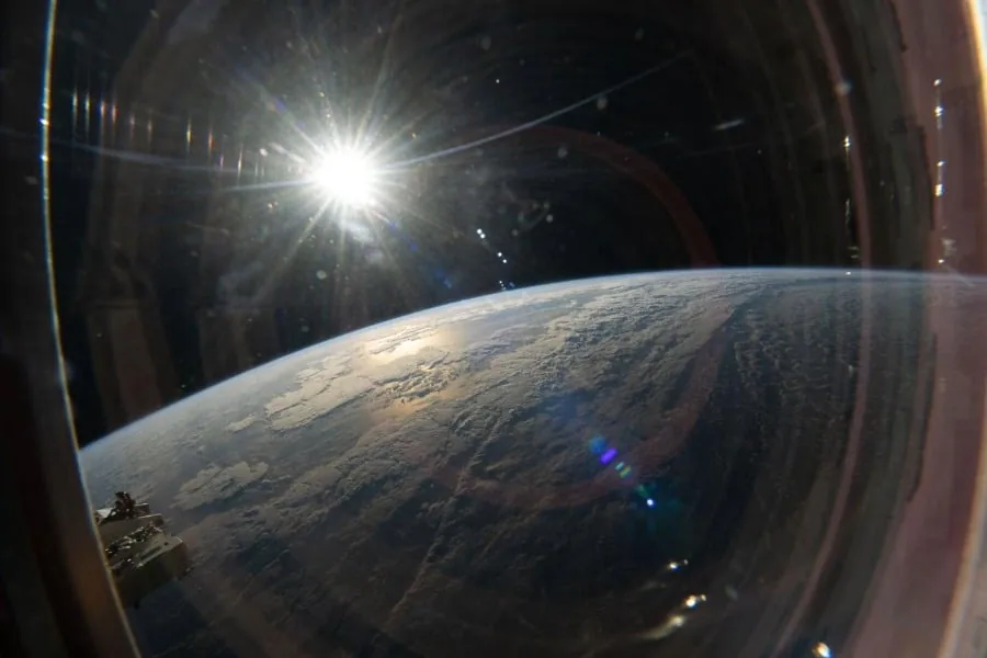 Vista panorámica de la curvatura de la Tierra con el sol brillando intensamente desde una escotilla espacial.