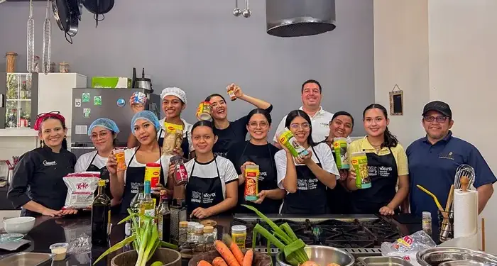Grupo diverso de personas sonriendo y sosteniendo productos en una cocina profesional equipada.