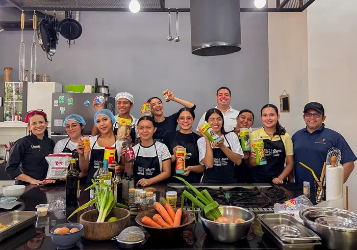 Grupo diverso de personas sonriendo y sosteniendo productos en una cocina profesional equipada.