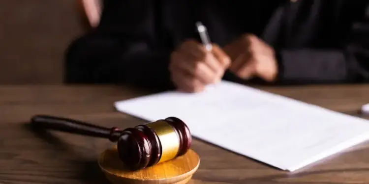 Un juez firmando un documento legal en una mesa de madera con un mazo de justicia en primer plano.