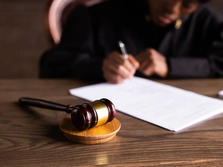 Un juez firmando un documento legal en una mesa de madera con un mazo de justicia en primer plano.
