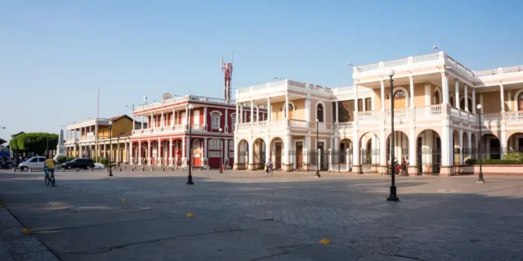 Vista panorámica de una plaza adoquinada con edificios coloniales de dos pisos, balcones con columnas y fachadas coloridas bajo un cielo despejado.