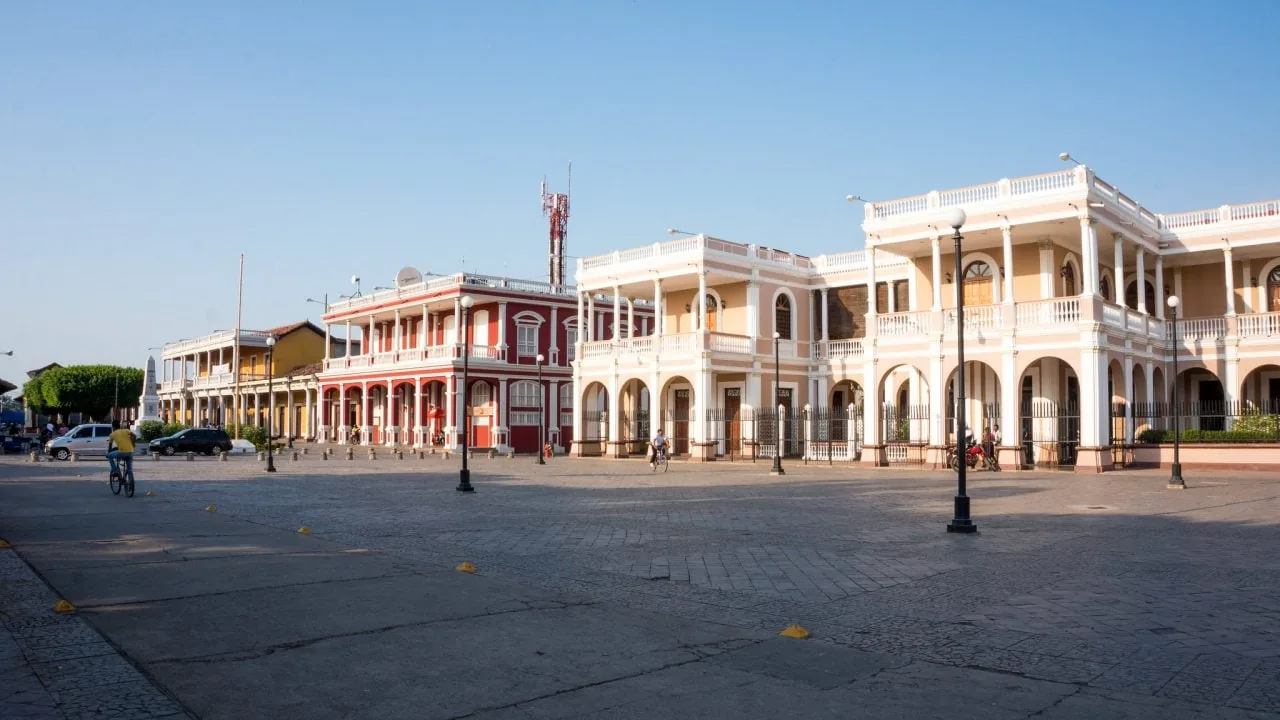 Vista panorámica de una plaza adoquinada con edificios coloniales de dos pisos, balcones con columnas y fachadas coloridas bajo un cielo despejado.
