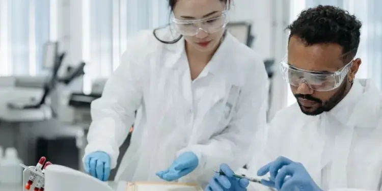 Dos científicos con bata blanca y gafas de protección trabajando en un laboratorio analizando muestras.