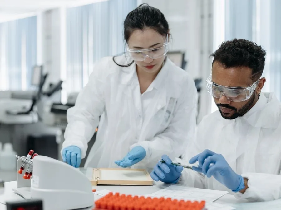 Dos científicos con bata blanca y gafas de protección trabajando en un laboratorio analizando muestras.
