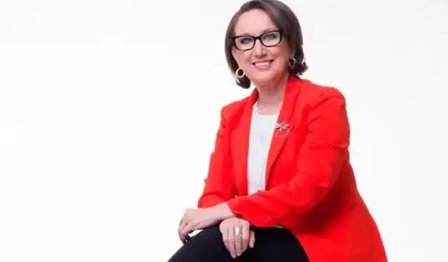 Mujer profesional sonriendo, vistiendo chaqueta roja y gafas, sentada sobre fondo blanco.