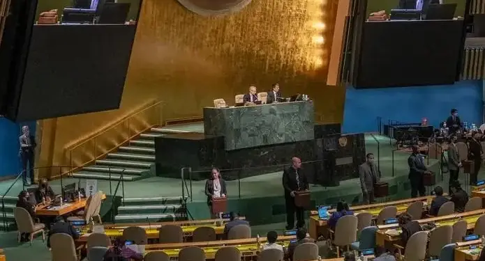 Oradores en un podio frente a una audiencia en una sala de conferencias internacional, con pantallas mostrando presentaciones.