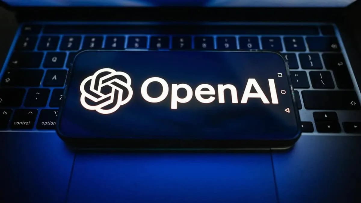 Logotipo de OpenAI y su nombre en pantalla de un smartphone colocado sobre el teclado de un portátil, simbolizando la integración de la inteligencia artificial en el mundo empresarial.