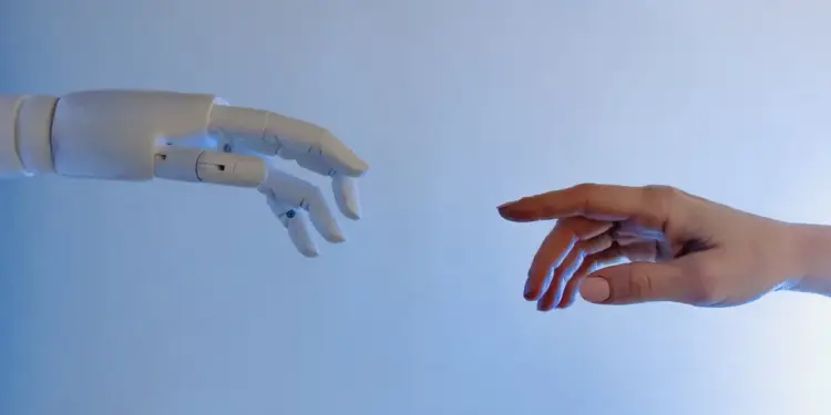 Mano humana y mano de un robot extendidas una hacia la otra sobre un fondo azul claro.