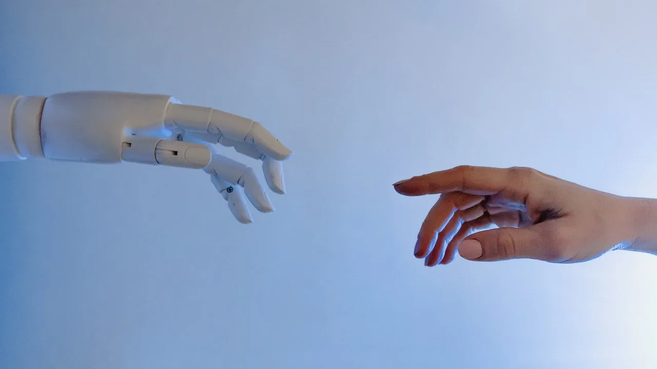 Mano humana y mano de un robot extendidas una hacia la otra sobre un fondo azul claro.