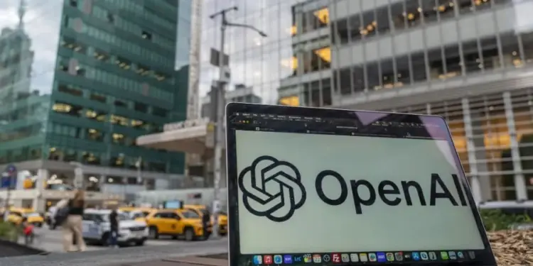Primer plano de una laptop mostrando el logo de OpenAI, con edificios de oficinas modernos y taxis amarillos en el fondo, representando el entorno empresarial y tecnológico.