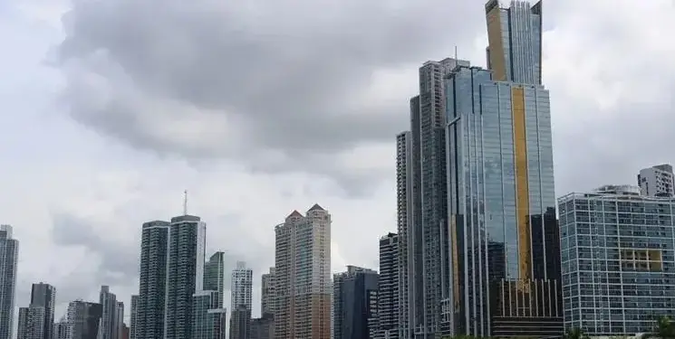 Vista panorámica de un horizonte urbano con numerosos rascacielos modernos de cristal y hormigón, bordeando una bahía bajo un cielo nublado. Refleja un centro de negocios.
