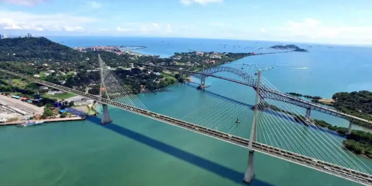 Vista aérea de dos puentes sobre aguas costeras, conectando tierra firme con una ciudad y un puerto. Refleja infraestructura y comercio.