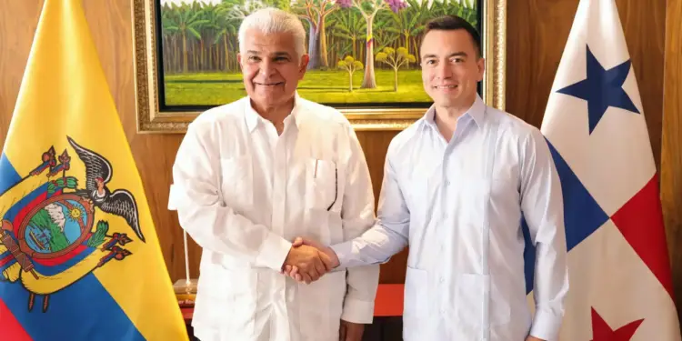 Dos hombres con camisas formales estrechan sus manos frente a banderas institucionales y una pintura al óleo.