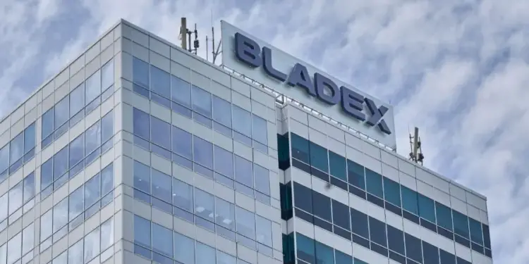 Vista angular de un moderno edificio corporativo con fachada de cristal y el letrero 'BLADEX' en la azotea bajo un cielo nublado.