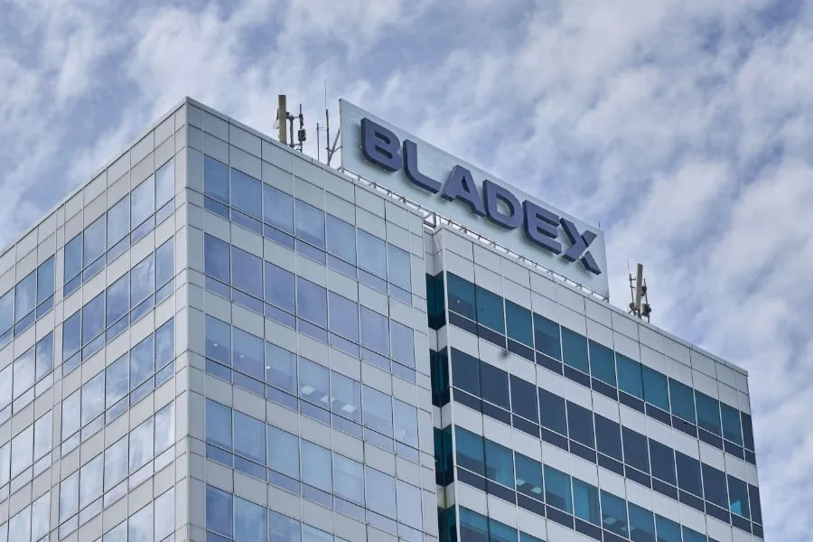 Vista angular de un moderno edificio corporativo con fachada de cristal y el letrero 'BLADEX' en la azotea bajo un cielo nublado.