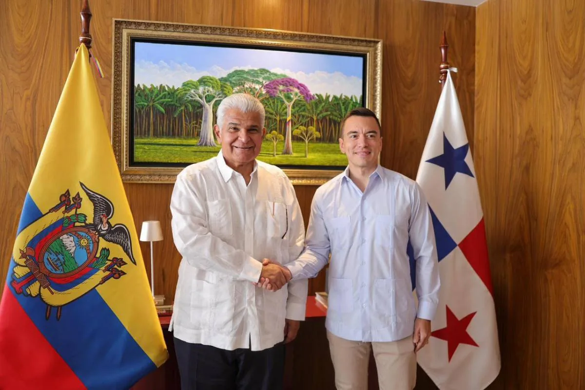 Dos hombres sonrientes estrechan manos frente a las banderas de Ecuador y Panamá, simbolizando un acuerdo o colaboración.