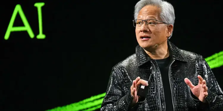 Hombre de cabello plateado con chaqueta negra brillante hablando en un evento corporativo de inteligencia artificial.