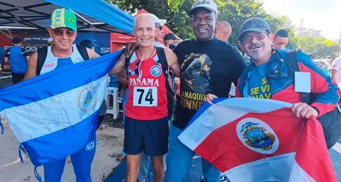 Grupo de cuatro atletas sonrientes sosteniendo banderas nacionales en un evento al aire libre.
