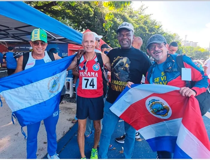 Grupo de cuatro atletas sonrientes sosteniendo banderas nacionales en un evento al aire libre.