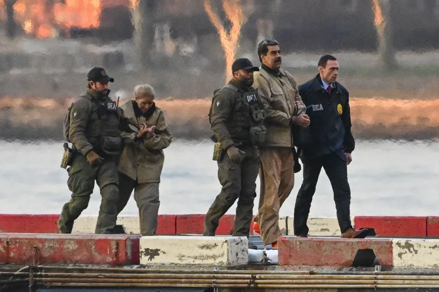 Un grupo de agentes tácticos escoltando a varias personas esposadas en un muelle.