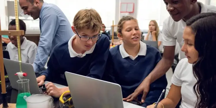 Estudiantes y adultos colaboran en un laboratorio, usando laptops y equipos científicos. Foco en el aprendizaje interactivo y tecnológico.